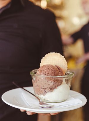 Eis mit Waffel im Glasbecher und ein langer Eis-Löffel, dazu eine Serviette, platziert auf einem kleinen Teller, serviert von einem Kellner im schwarzen Hemd