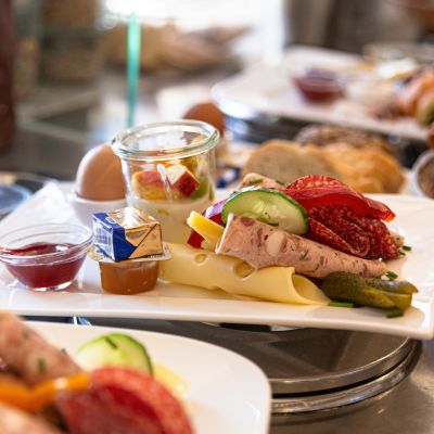 Frühstücksteller mit Wurst, Käse, Butter, Marmelade und Ei, sowie Brötchen und Croissants